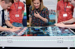 TV personality, Caroline Flack watching two players participating on the Neuron Race reaction game.