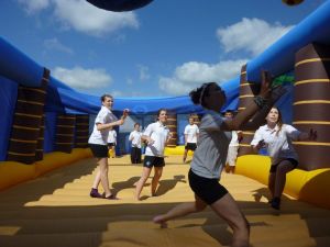 A group of boys and girls playing bouncy volleyball inside the inflatable sports arena court at a school activity day.