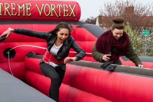 Two girls with bean bags in their hands as they run along the inflatable bungee run game.