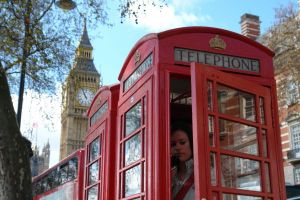 A person standing in a London phone box making a telephone call with Big Ben in the background.