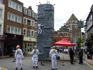 Mobile rock climbing wall set up in Kingston high street with people climbing and morris dancers watching them.