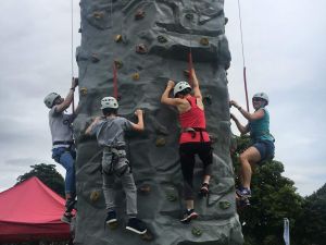 Four rock climbers ascending the portable rock climbing tower at a family fun day event.