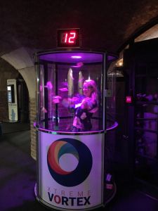 A lady competing inside a Grab A Grand machine where she is trying to grab the tokens as they are blown around in the cash cylinder.