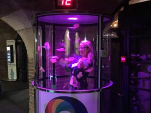 A lady competing inside a Grab A Grand machine where she is trying to grab the tokens as they are blown around in the cash cylinder.