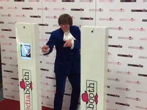 Austin Powers lookalike standing in front of a Social Media Pod having his photo taken.
