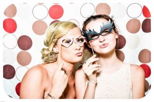 Two girls standing in a photo booth having their photo taken with props in their hand.